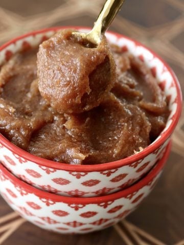 Date butter in a red-rimmed bowl on a dark wood cutting board, with a tiny gold spoon.