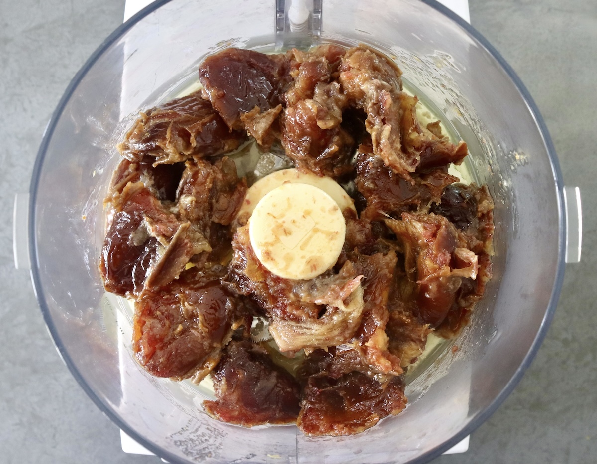 Hydrated dates with melted butter in a food processor bowl.
