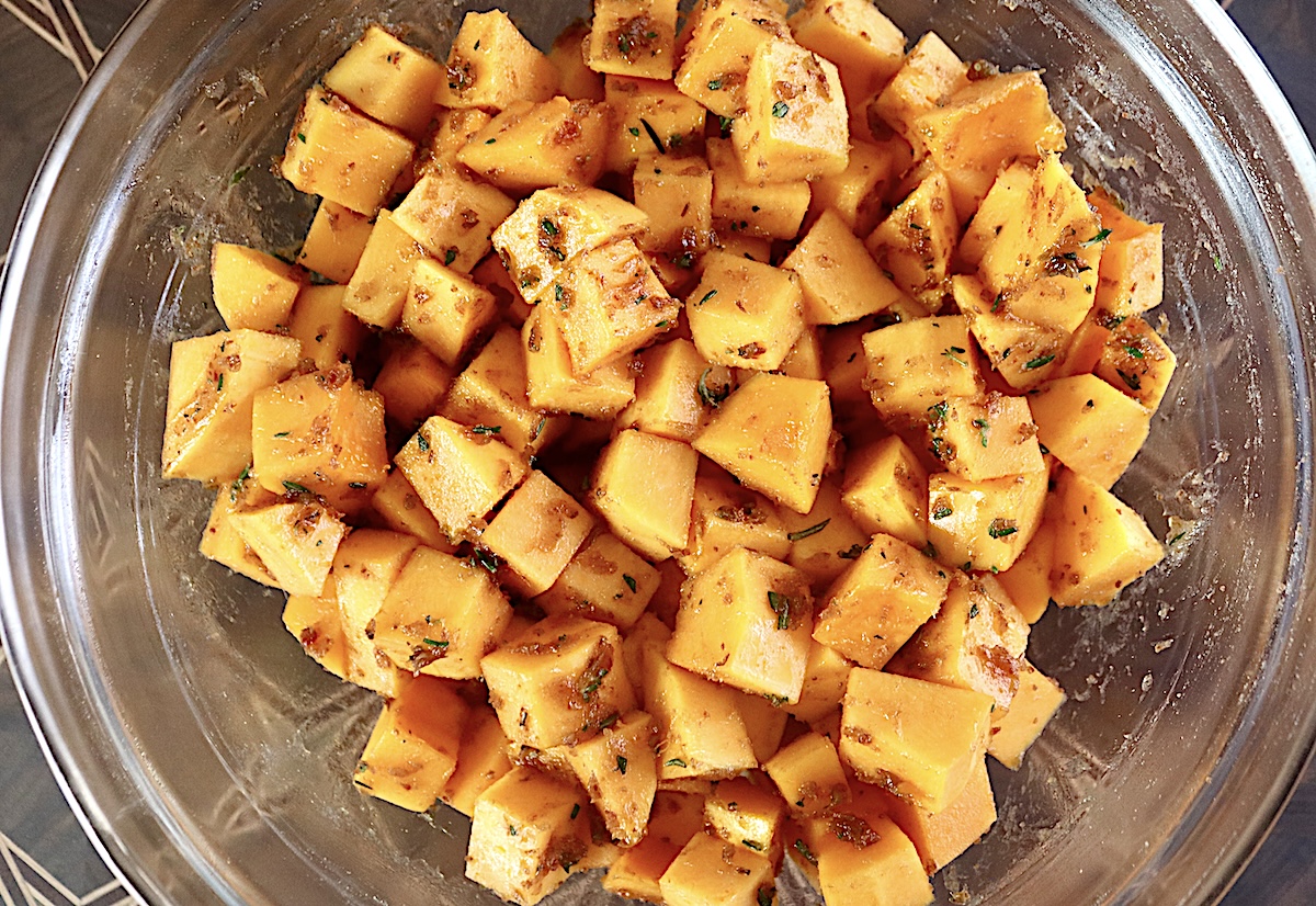 Pile of raw butternut squash cubes mixed with date butter and fresh herbs.