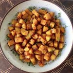 Top view of a cream-colored, brown-rimmed ceramic bowl filled with chunks or roasted butternut squash.