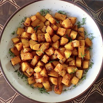 Top view of a cream-colored, brown-rimmed ceramic bowl filled with chunks or roasted butternut squash.