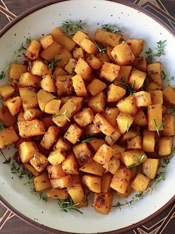 Top view of a cream-colored, brown-rimmed ceramic bowl filled with chunks or roasted butternut squash.