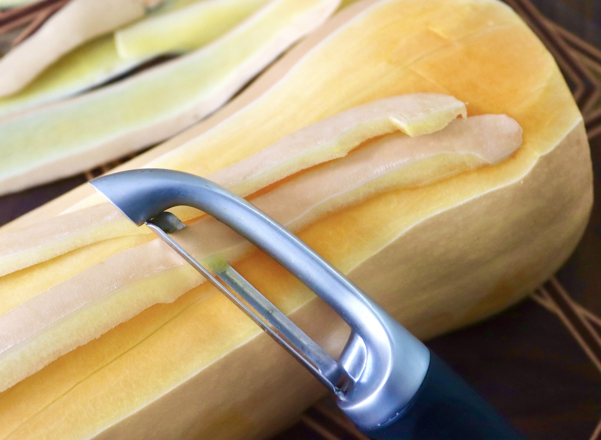 Butternut squash being peeled with a vegetable peeler.