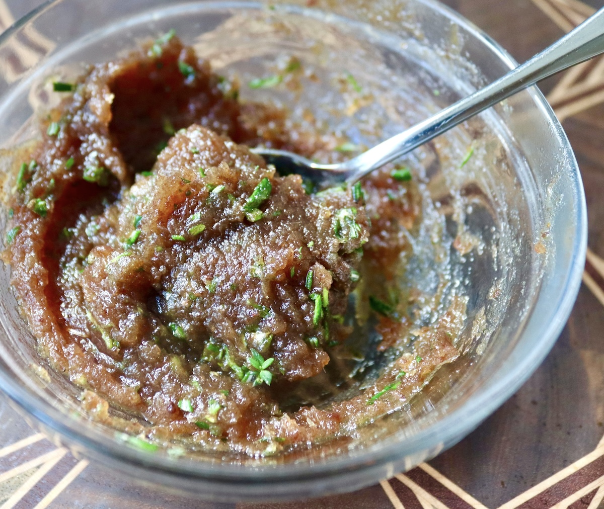 Small glass bowl with date paste mixed with fresh herbs.