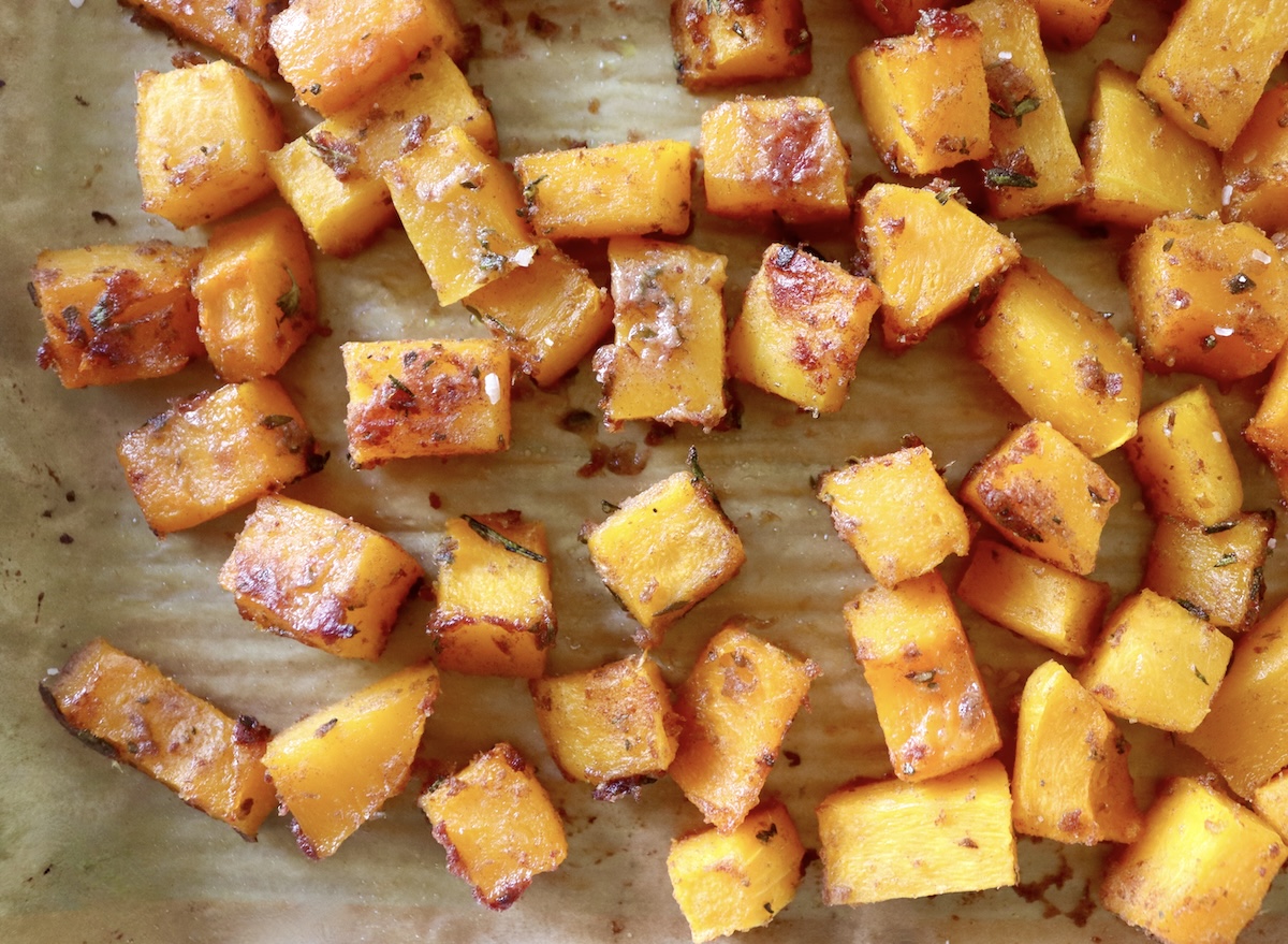 Close up of roasted butternut squash cubes coated with date butter and fresh herbs.