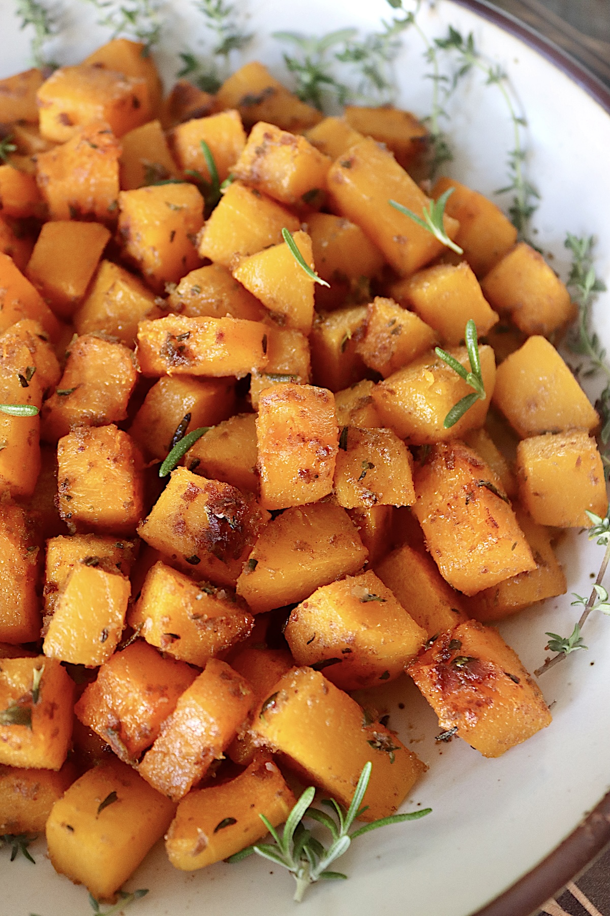 Date Roasted Butternut Squash cut into cubes with fresh herbs on a white platter.