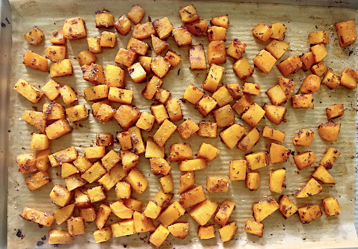 Sheet pan with roasted butternut squash cubes coated with date butter and fresh herbs.