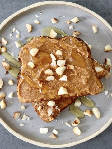 Two pieces of toast on top of each other with macadamia nut butter, and chopped nuts around it.