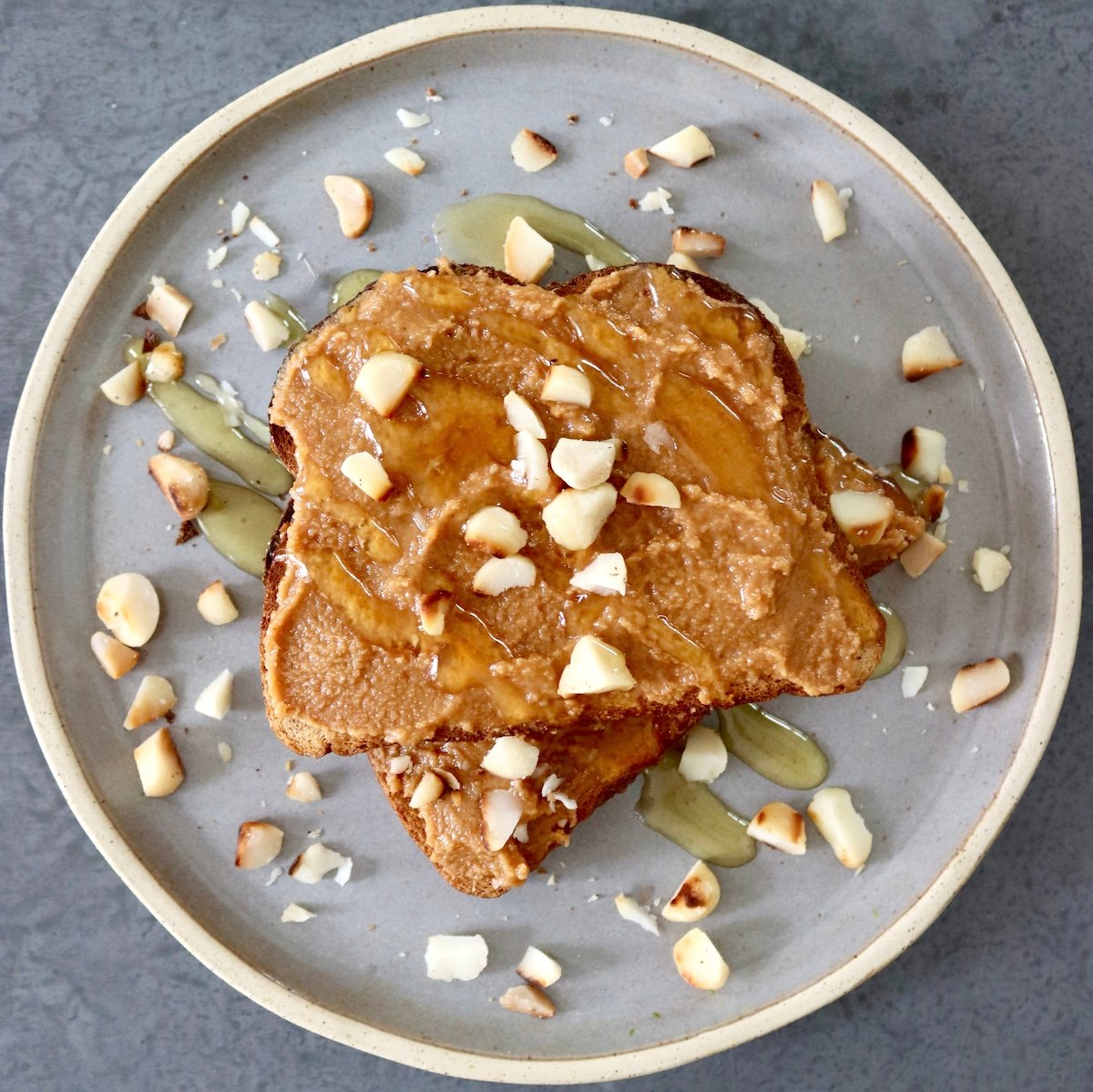 Two pieces of toast on top of each other with macadamia nut butter, and chopped nuts around it.