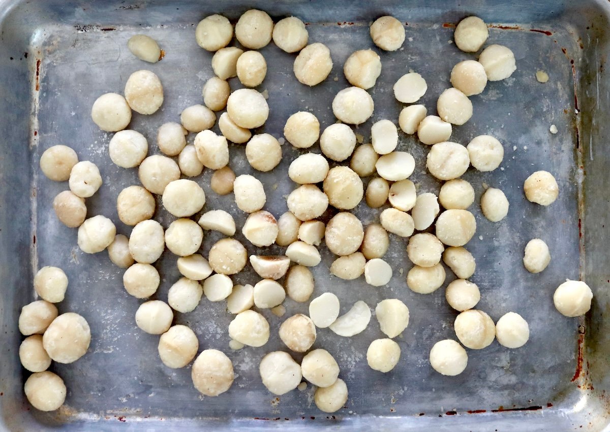 Small sheet pan filled with raw macadamia nuts.