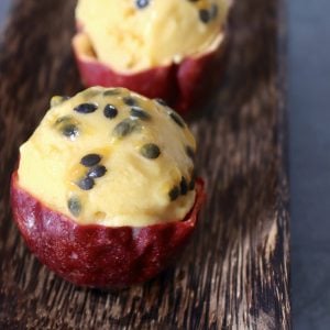 Passion fruit ice cream scooped into three individual halved passion fruit skins, with the seeds on top.