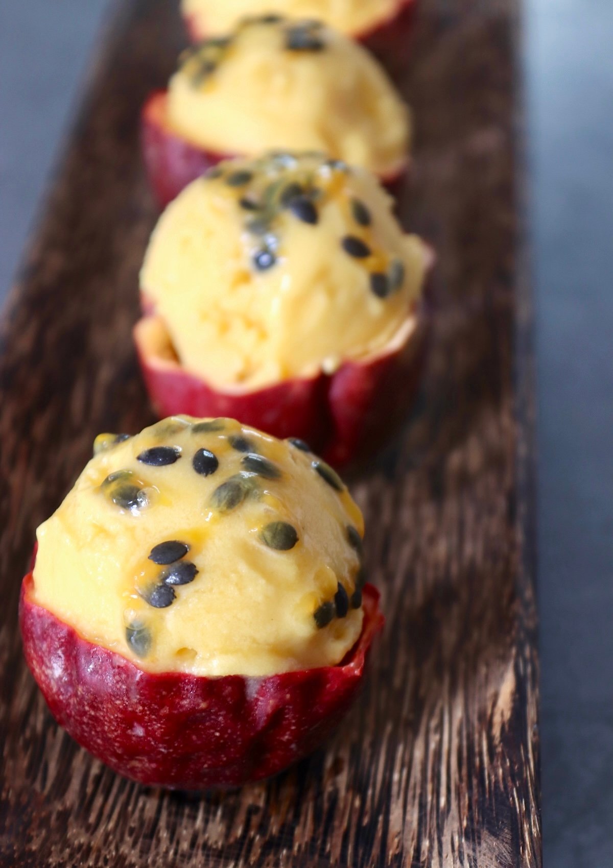 Passion fruit ice cream scooped into three individual halved passion fruit skins, with the seeds on top.