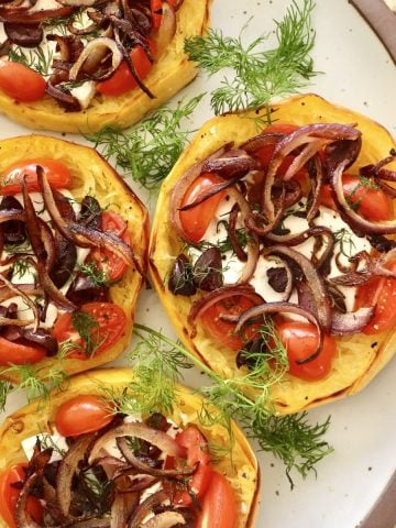 One side of a round platter with 4 spaghetti squash tiny pizzas with fresh dill in between.