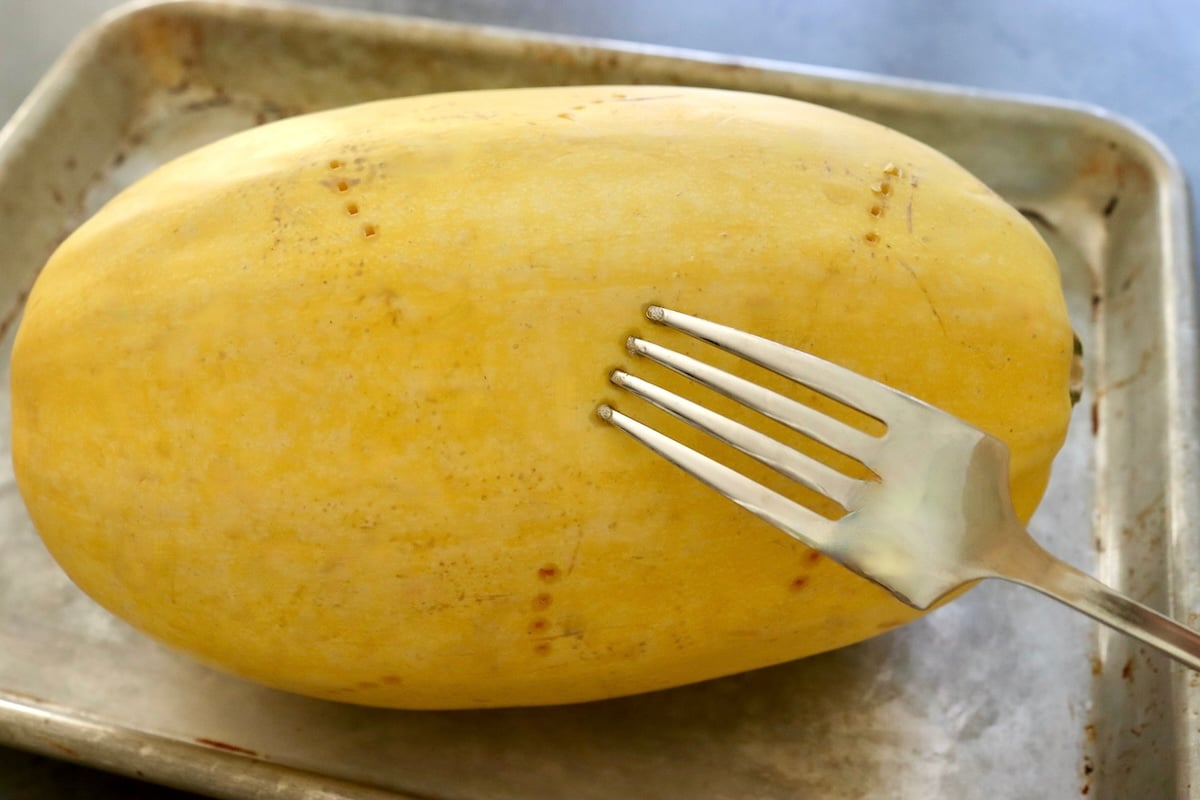 Spaghetti-Squash-Rings-with-Feta-and-Olives Large spaghetti squash with a fork poking holes in it.