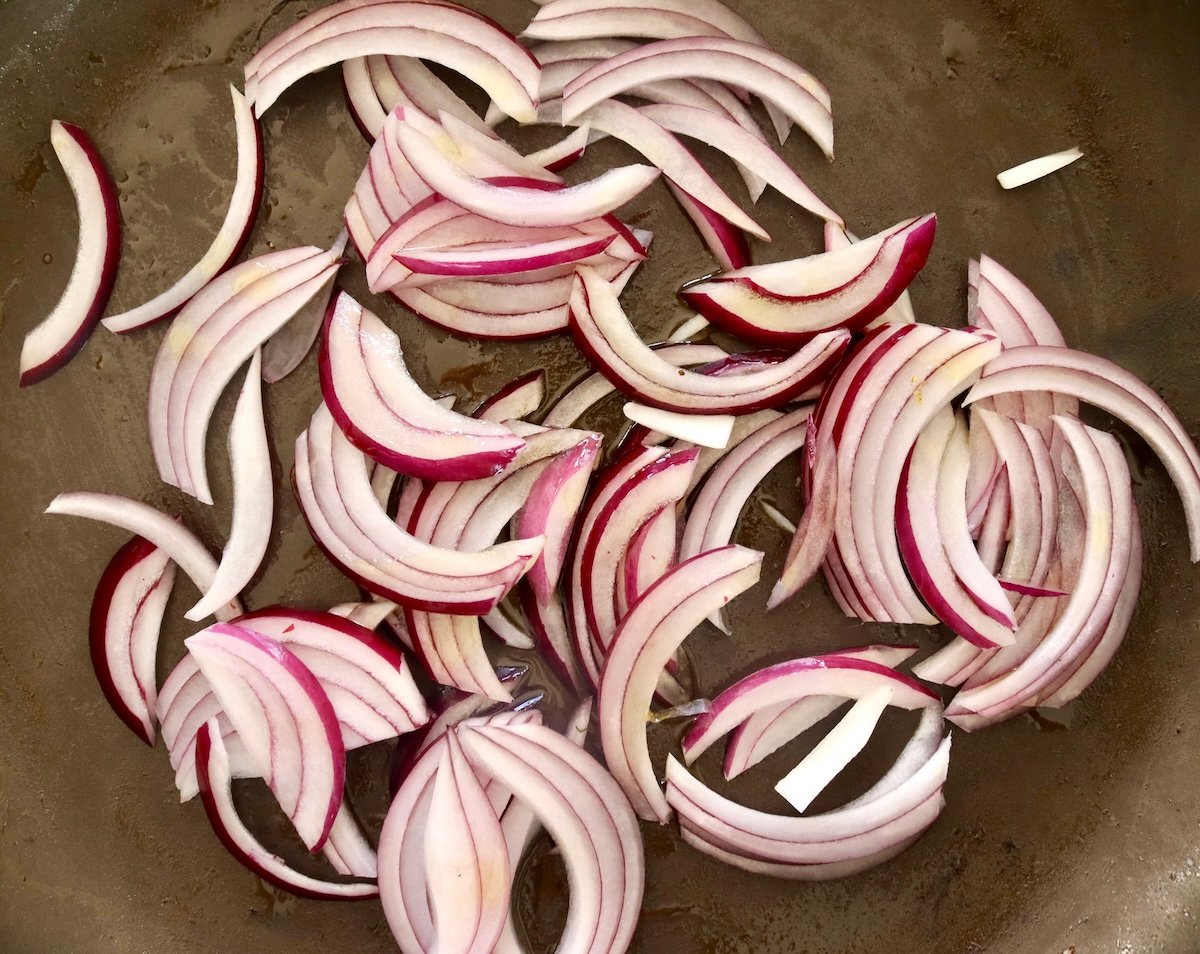 Spaghetti-Squash-Rings-with-Feta-and-Olives Raw red onion slices in a skillet.
