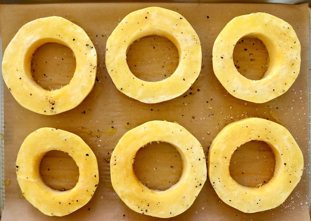 Spaghetti-Squash-Rings-with-Feta-and-Olives 6 raw spaghetti squash rings on a sheet pan with parchment paper, with olive oil and salt and pepper.