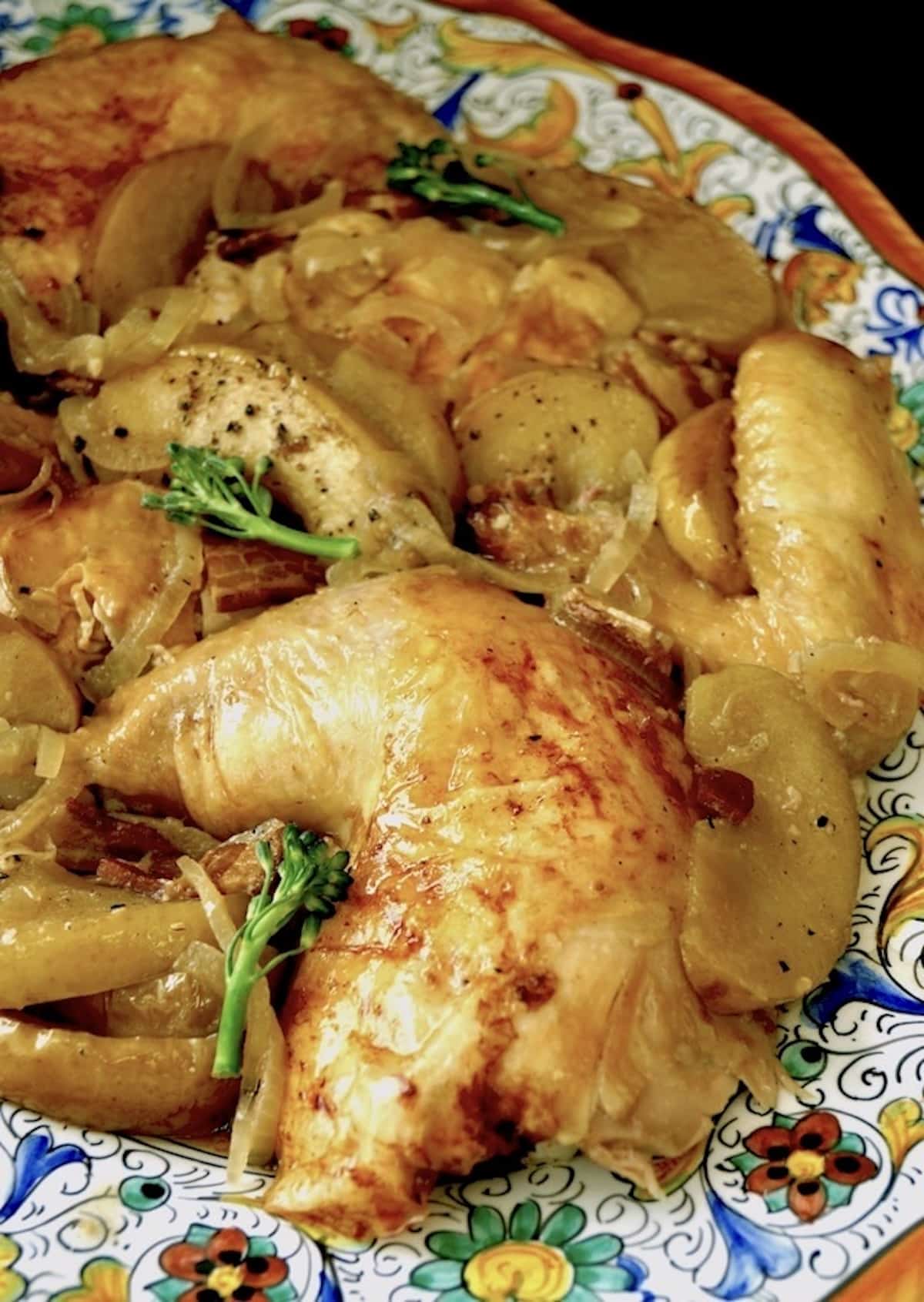 Cut up whole roasted chicken with apple and onion slices on an Italian platter.