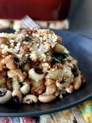 Black plate with a serving of black-eyed pea casserole, with a red baking pan behind it.