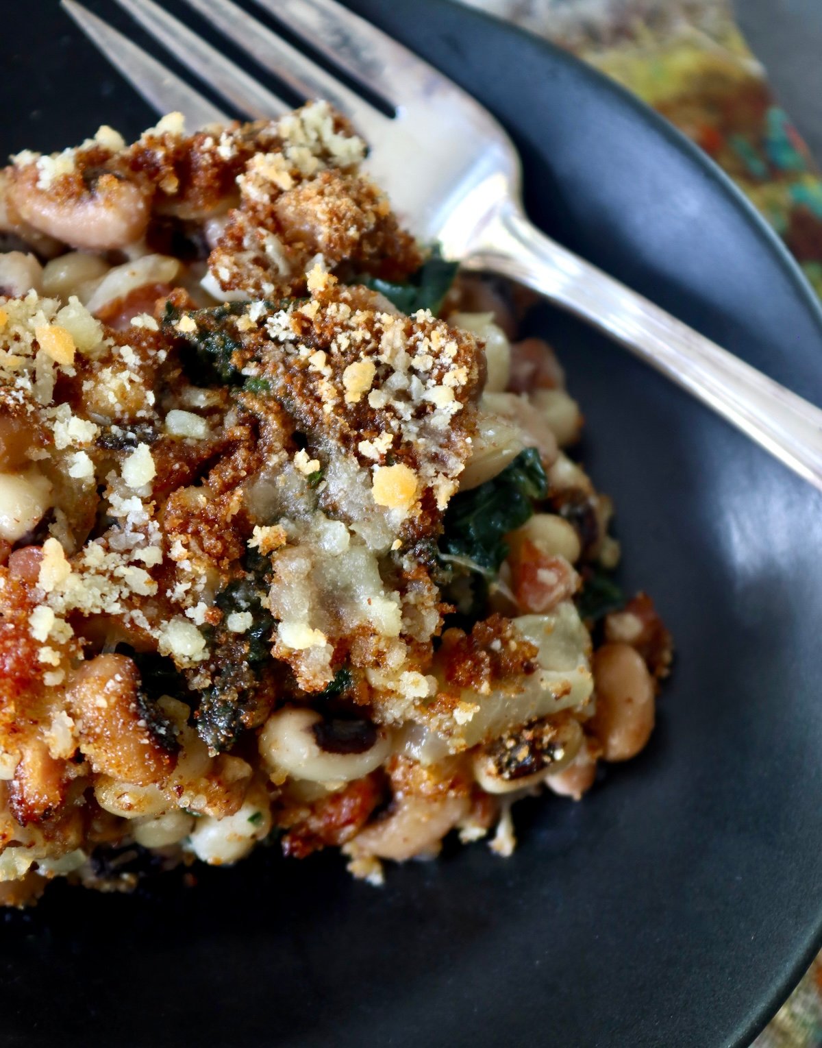 Black-Eyed Pea Casserole Top view of a browned black-eyed casserole on a black plate with a fork.