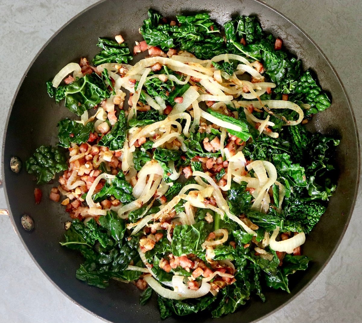 Black-Eyed Pea Casserole Skillet with diced pancetta, sliced onions and wilted kale.
