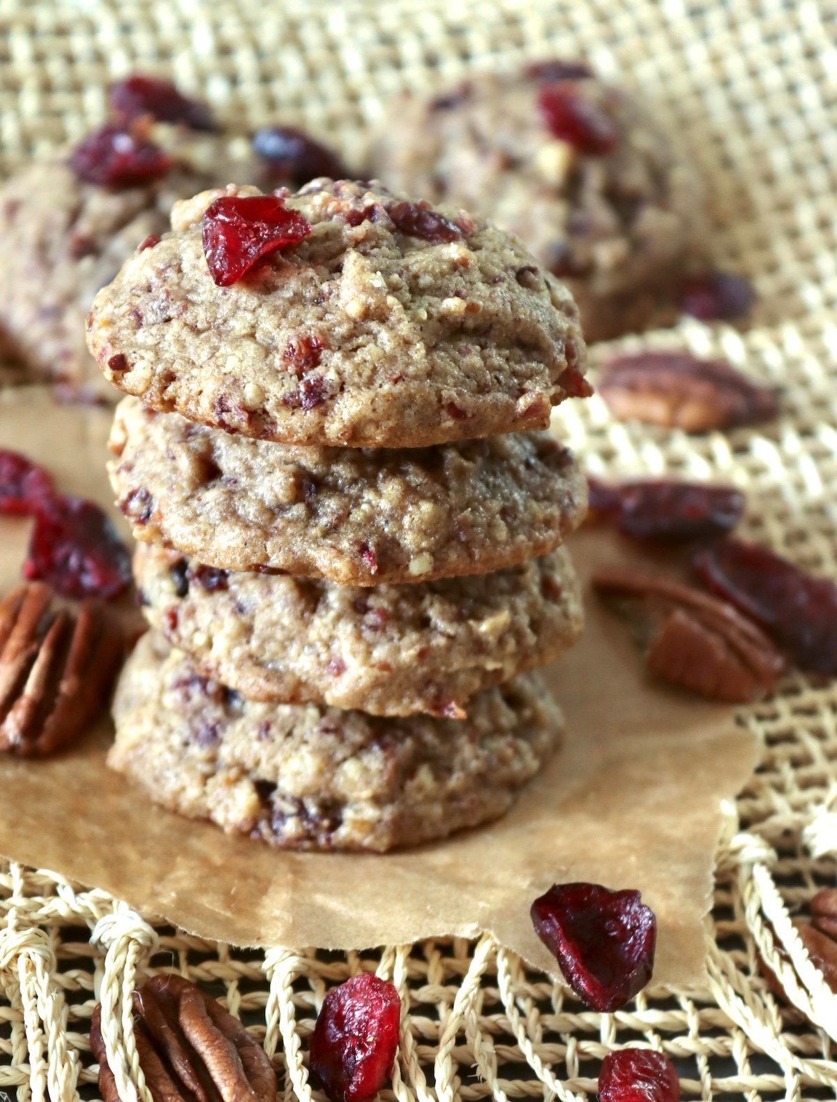 Stack of 4 pecan cranberry cookies with orange, with a few dried cranberries and pecan halves around them.