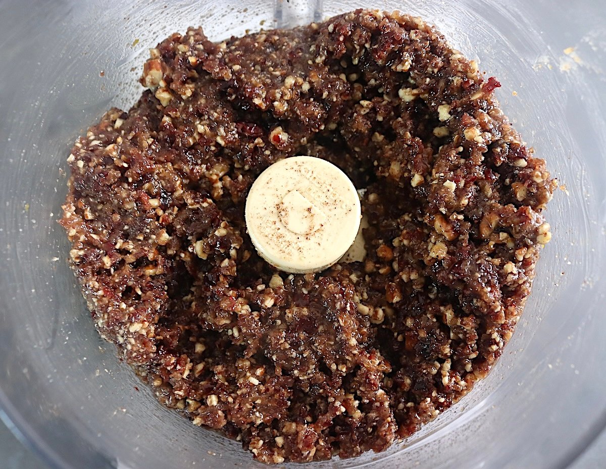 Paste-like mixture of pecans and dried cranberries in a food processor bowl.