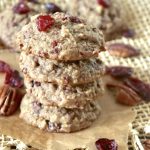 Stack of 4 pecan cranberry cookies with orange, with a few dried cranberries and pecan halves around them.