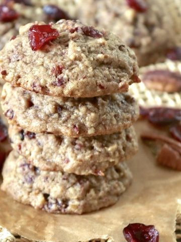 Stack of 4 pecan cranberry cookies with orange, with a few dried cranberries and pecan halves around them.