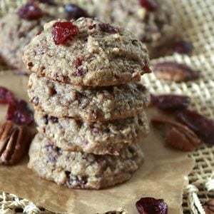Stack of 4 pecan cranberry cookies with orange, with a few dried cranberries and pecan halves around them.