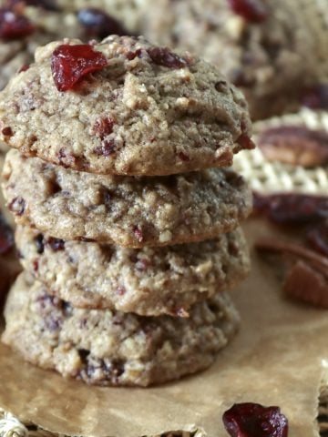 Stack of 4 pecan cranberry cookies with orange, with a few dried cranberries and pecan halves around them.