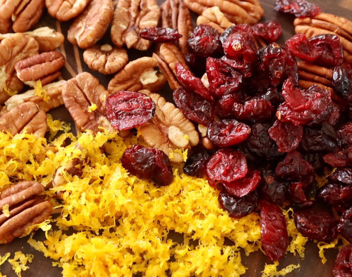 Pile of raw pecan halves, orange zest and dried cranberries.