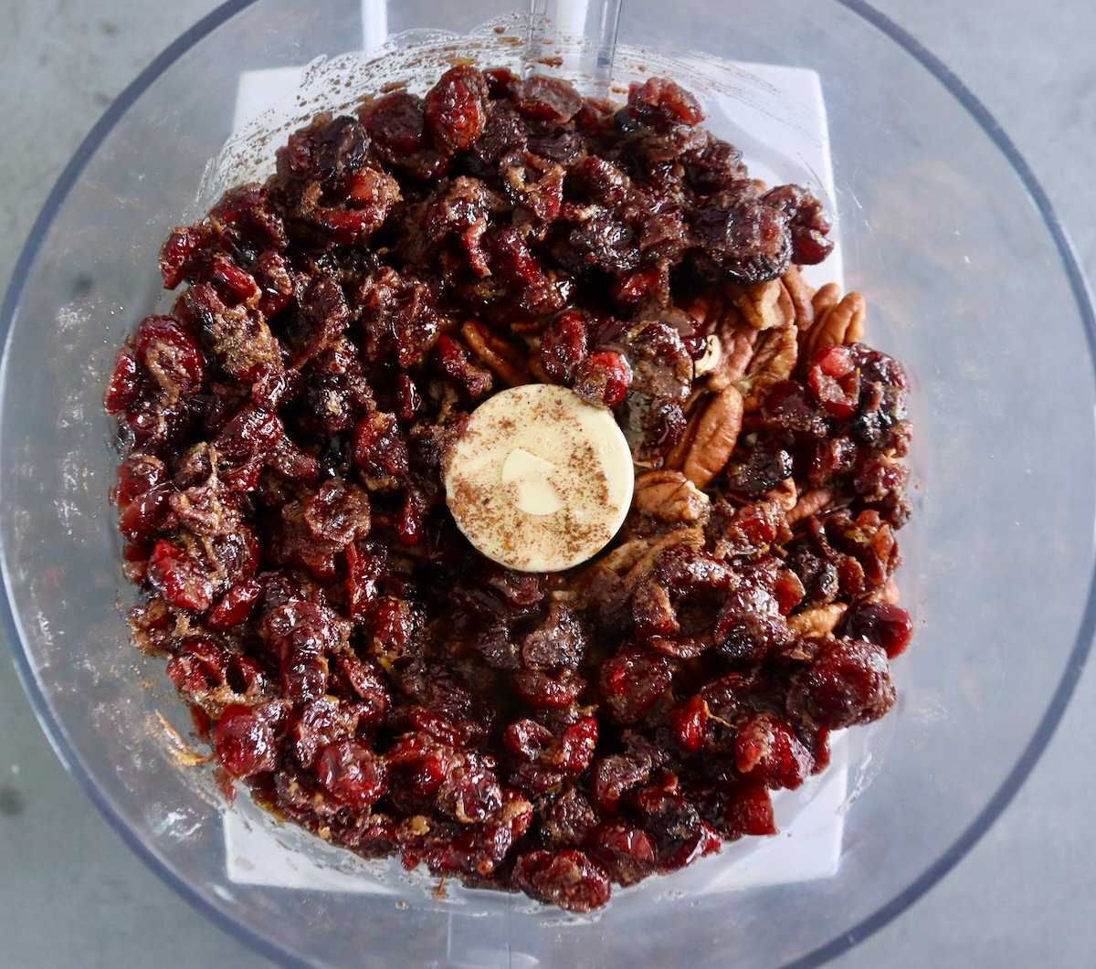 Dried cranberries soaked in melted butter with pecans and sugar in a food processor bowl.