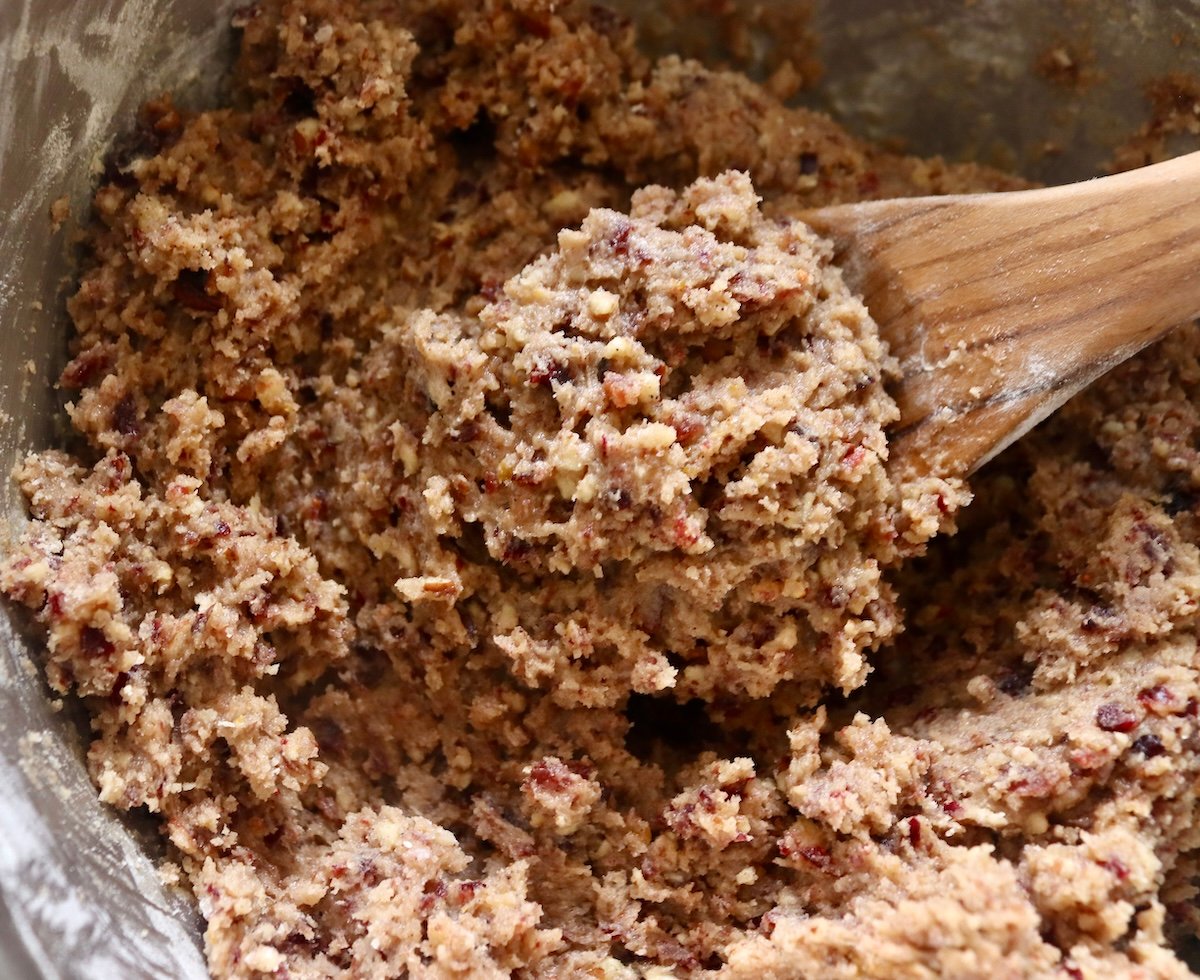 Pecan cranberry cookie batter in a mixing bowl with a wooden spoon.