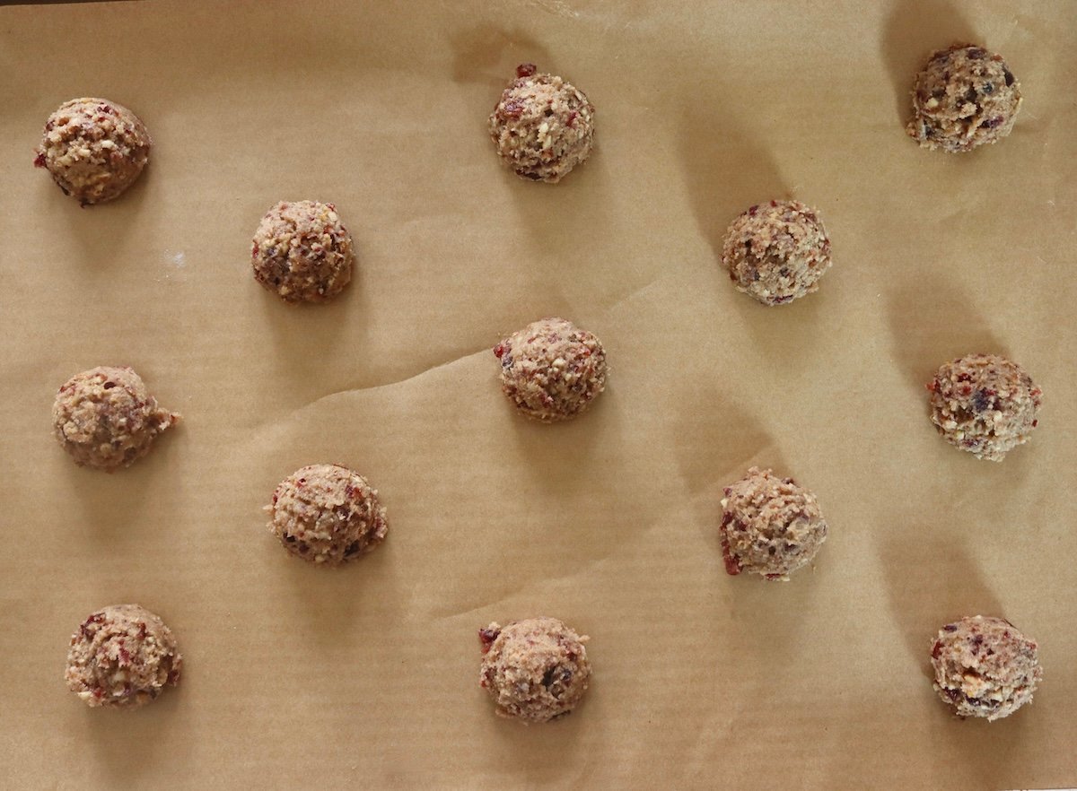 About 13 balls of pecan-cranberry cookie batter on a parchment-lined baking sheet.