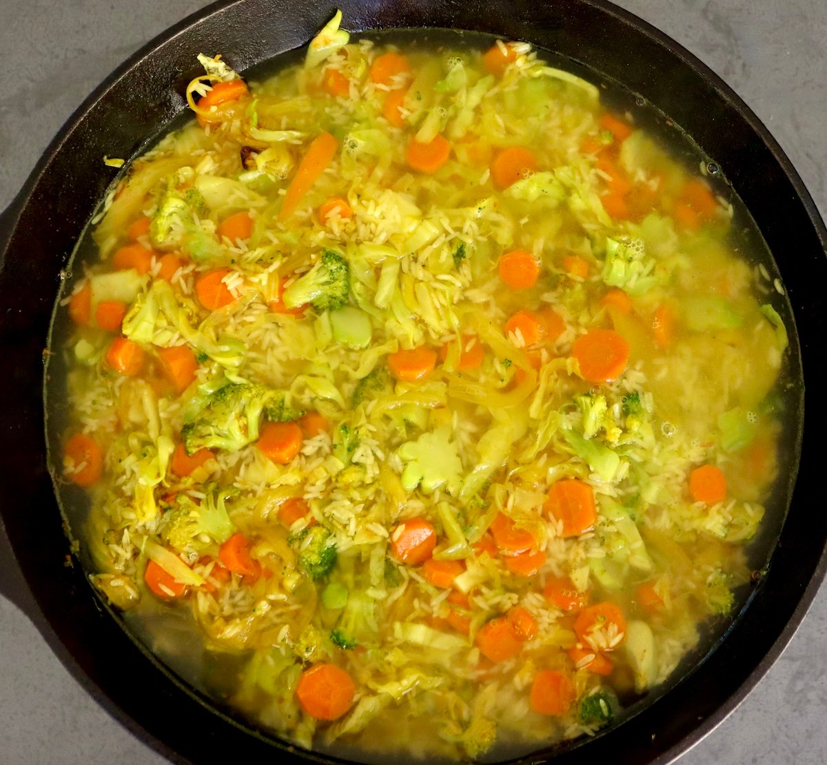 Baked-Red-Snapper-Recipe Large cast iron skillet filled with sauteed cabbage, broccoli, onion, carrots, rice and water.