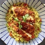 Top View of blue striped plate with yellow rice and sliced, red-spiced fish, with a sprig of cilantro.