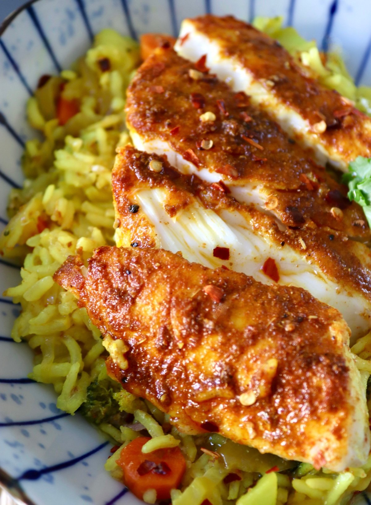 Baked-Red-Snapper-Recipe op View of blue striped plate with yellow rice and flaked, red-spiced fish..