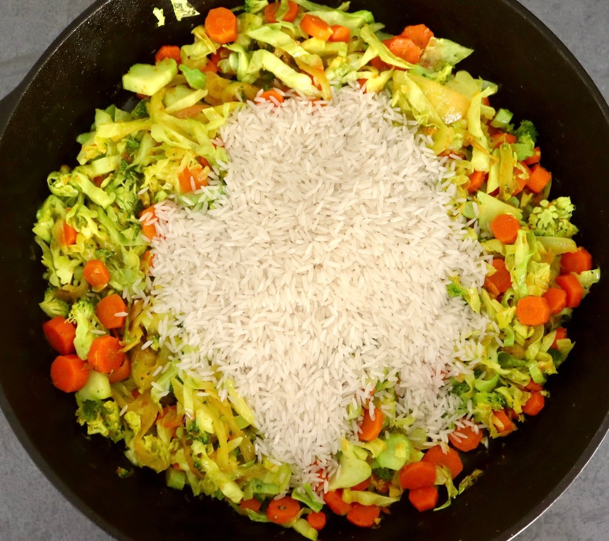 Baked-Red-Snapper-Recipe Large cast iron skillet filled with sauteed cabbage, broccoli, onion and carrots, and a pile of rice on top.