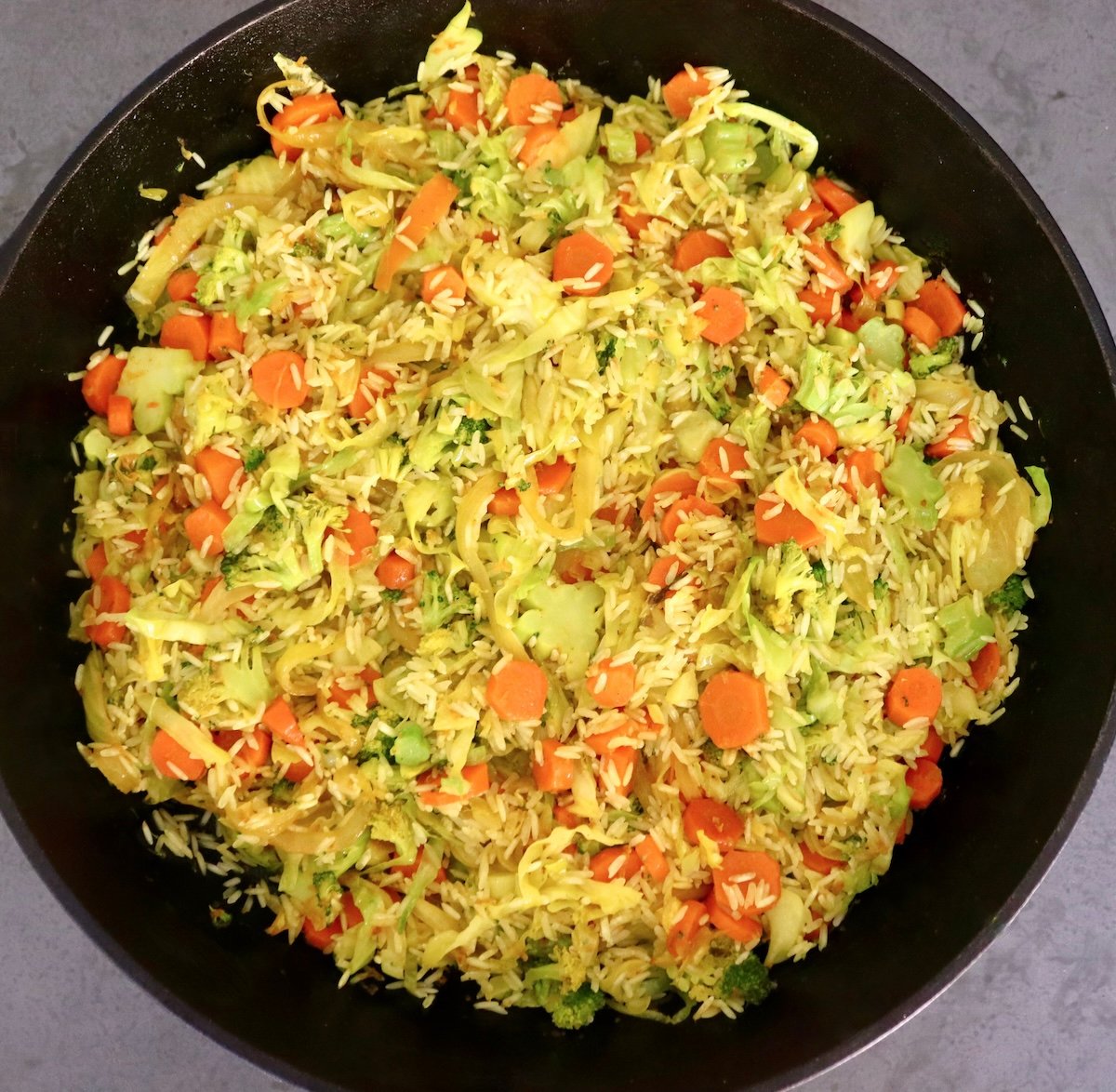 Baked-Red-Snapper-Recipe Large cast iron skillet filled with sauteed cabbage, broccoli, onion carrots and rice.