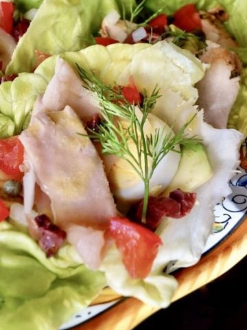 Italian painted plate with about a dozen small butter lettuce cups, filled with tuna, egg, tomatoe and olives.