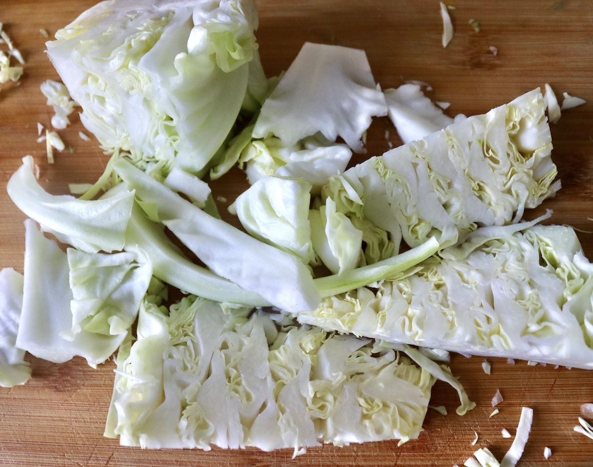 Core and root ends of green cabbage on a light wood cutting board.