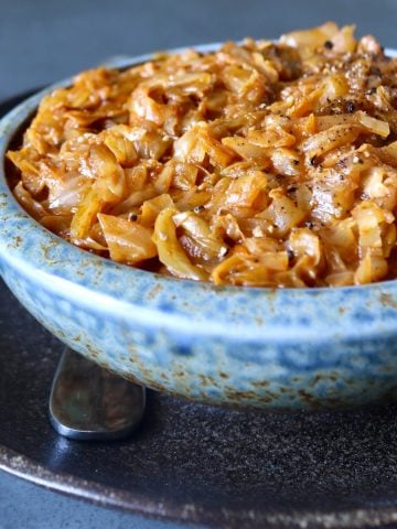 Light blue ceramic bowl full of tomato sautéed cabbage, on a dark brown ceramic plate.