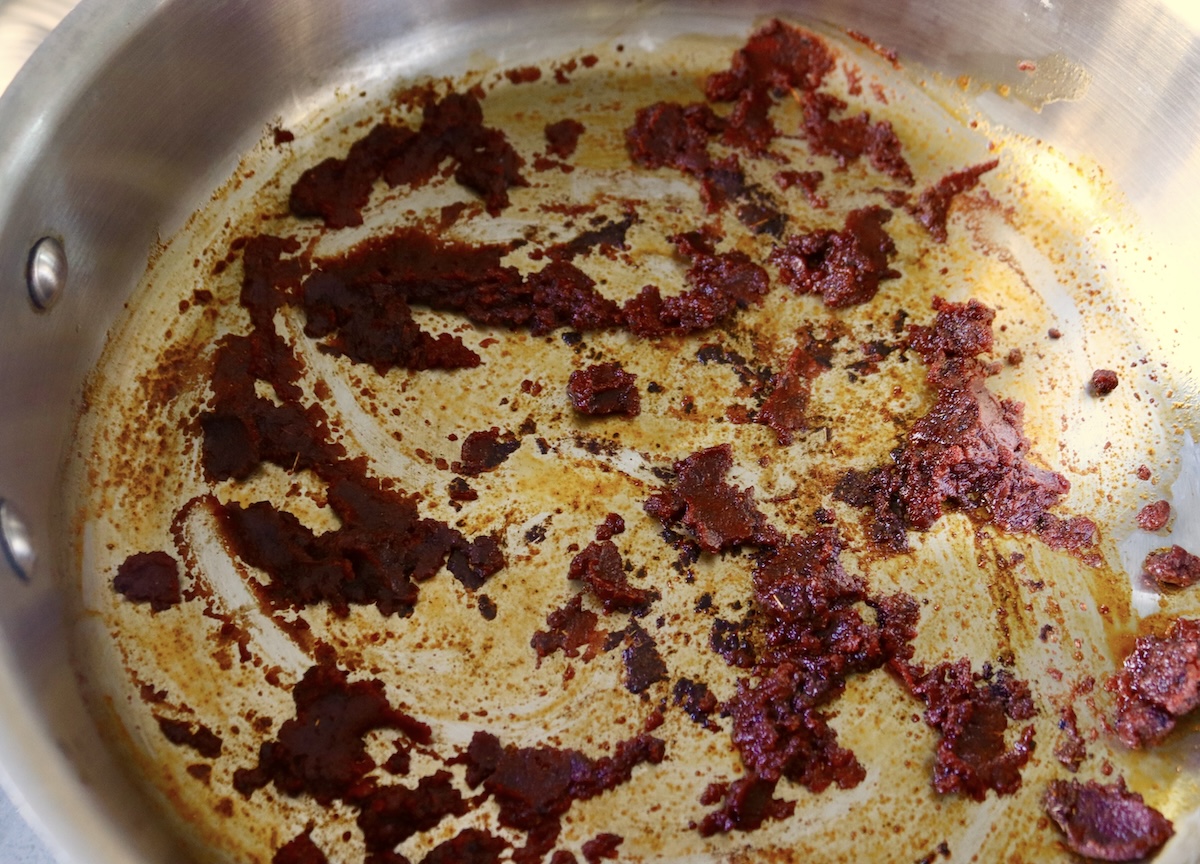 Browned tomato paste with spices in the bottom of a pan.