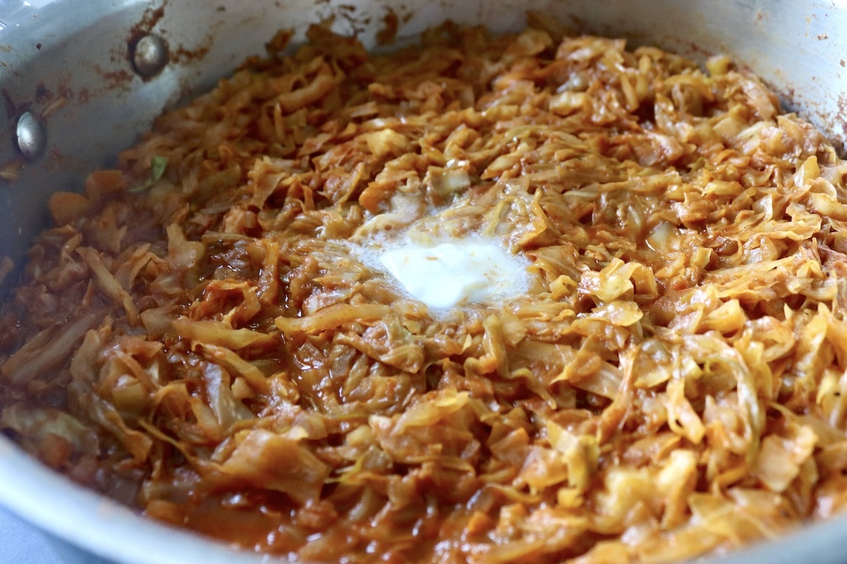 Sautéed and wilted cabbage with tomato sauce in a sauté pan with a melting pat of butter on top.