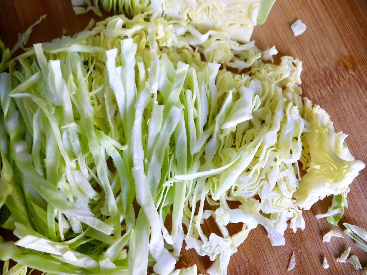 Pile of thinly sliced green cabbage on a cutting board.