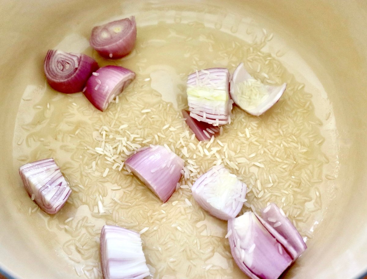 Edamame-Soup-Recipe Bottom of a Dutch oven with halved shallots, sprinkled raw rice and oil.