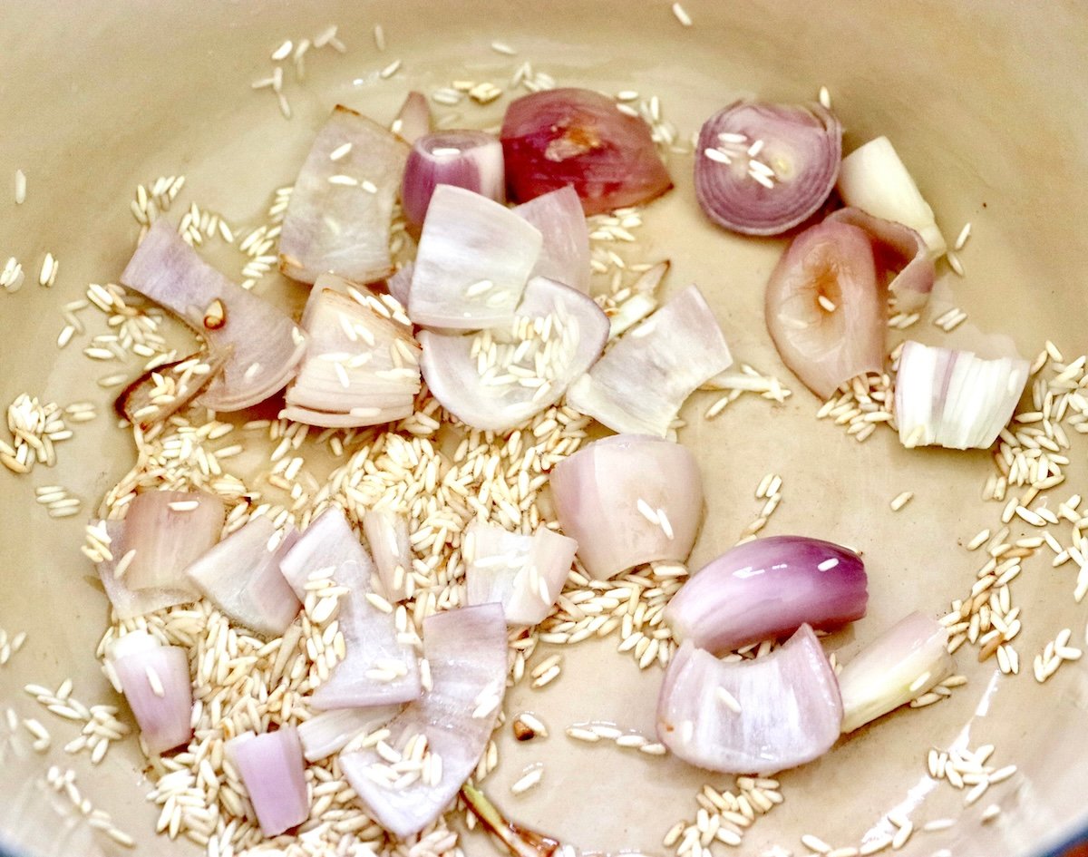 Edamame-Soup-Recipe Bottom of a Dutch oven with halved sautรฉed shallots, sprinkled golden rice and oil.