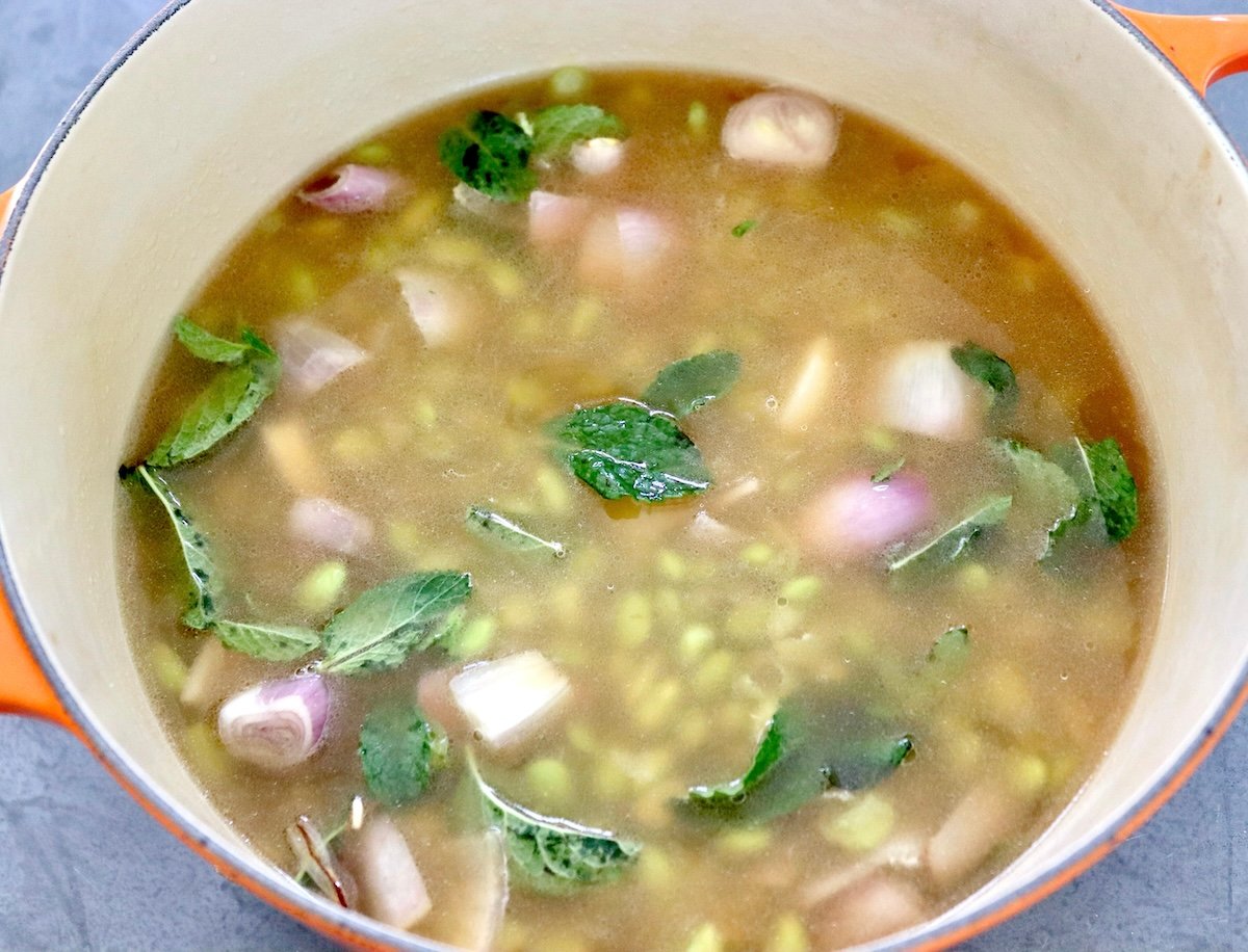 Edamame-Soup-Recipe Dutch oven full of edamame, shallots, mint leaves and vegetable stock.