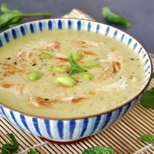Blue and white striped, ceramic bowl with edamame soup with chili oil, mint leaf, and a bit of cream.