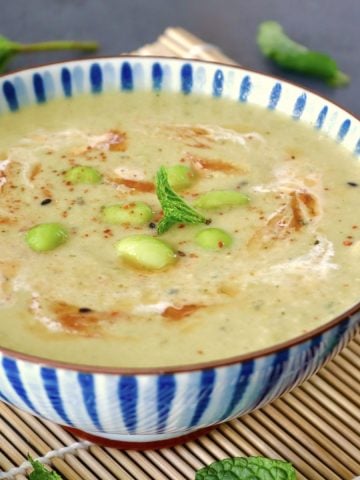 Blue and white striped, ceramic bowl with edamame soup with chili oil, mint leaf, and a bit of cream.